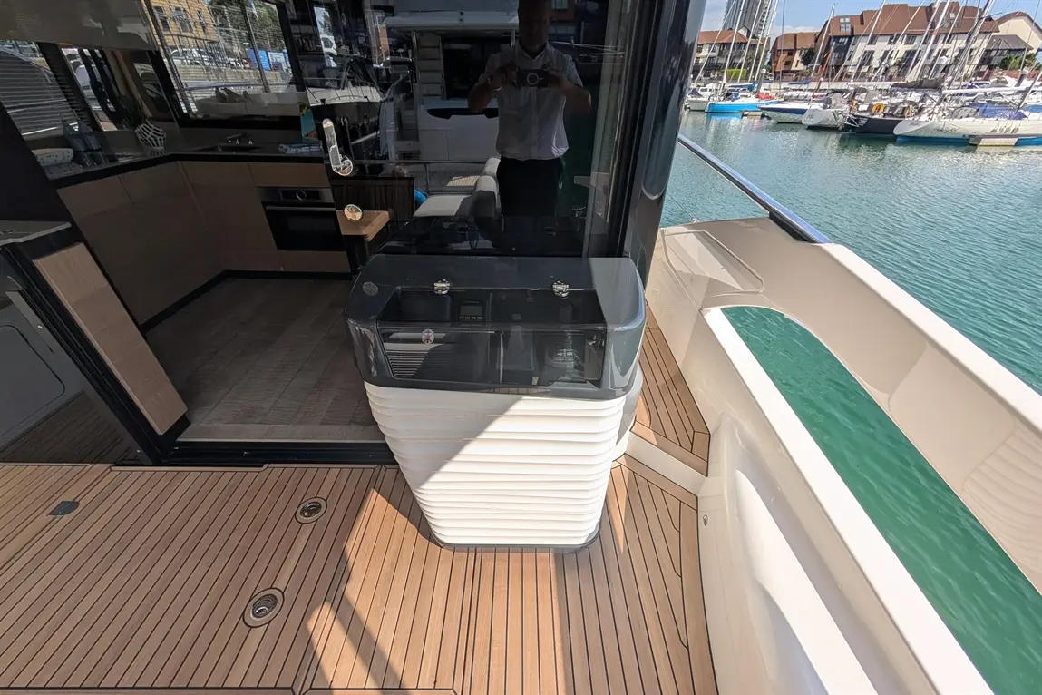 A modern yacht's deck showing a stylish outdoor kitchen unit, with a view of the marina and boats in the background.
